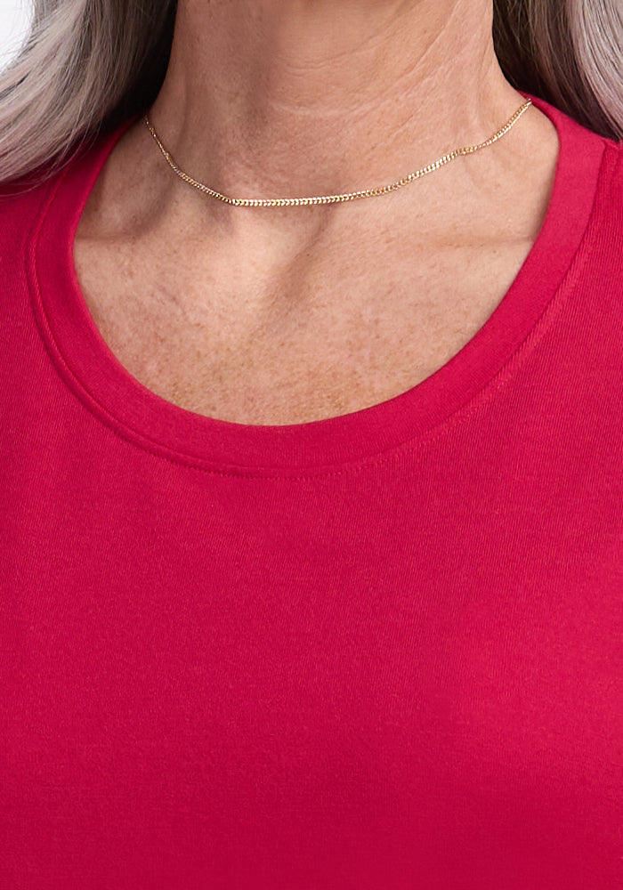 A close-up of a person wearing a gold chain necklace and the Woolx Georgie Dress in Poppy Spark, highlighting the neckline, collarbone, and upper chest.