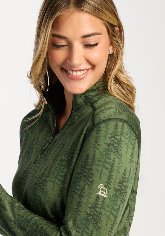 Woman smiling in Woolx Emi 1/4 Zip - Forest Friends, a green Merino base layer with tree pattern and moisture-wicking logo.