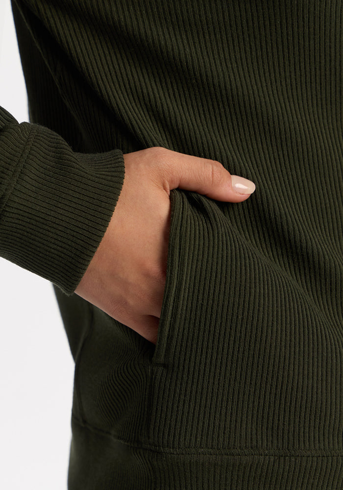 Close-up of a hand with light nail polish slipping into the pocket of the Woolx Quinn Ribbed 1/4 Zip - Duffel Bag.