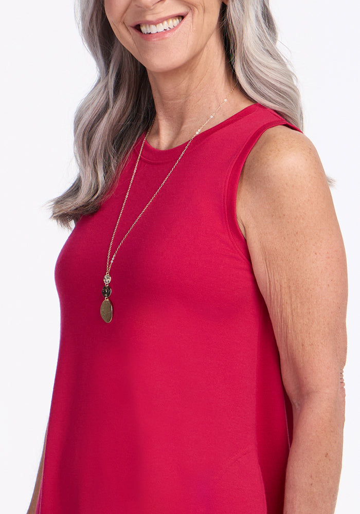 A smiling older woman with long gray hair wears the Woolx Clara Dress in Poppy Spark and a long necklace with round pendants, shown from the shoulders up against a plain white background.
