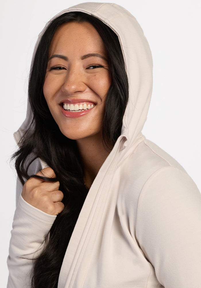 Woman smiles in the Woolx Zoey Zip Up Hoodie in Ecru, ideal for comfort and warmth.