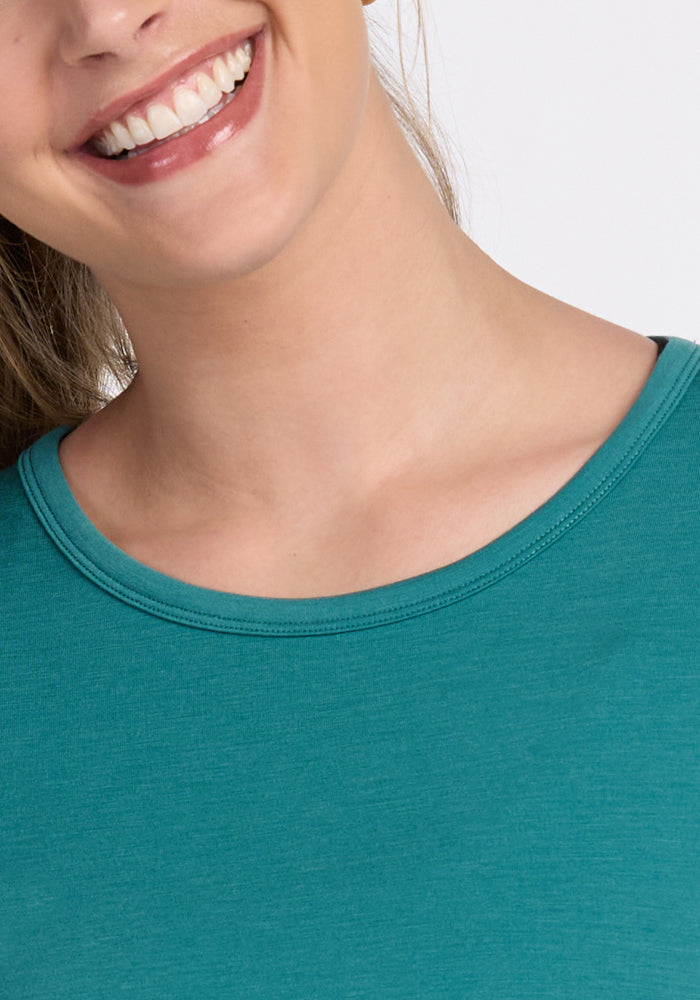 A close-up of a smiling woman wearing the Woolx Addie Crew Neck - Surfside. Only her lower face, neck, and upper chest are visible—highlighting this versatile women’s merino wool tee.