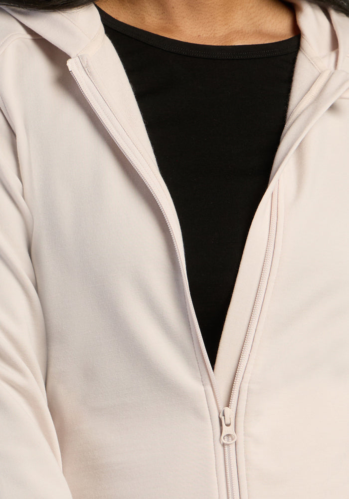 A woman layers a black shirt under the Woolx Darby Zip Up Hoodie in Ecru, partially unzipped for a chic look.
