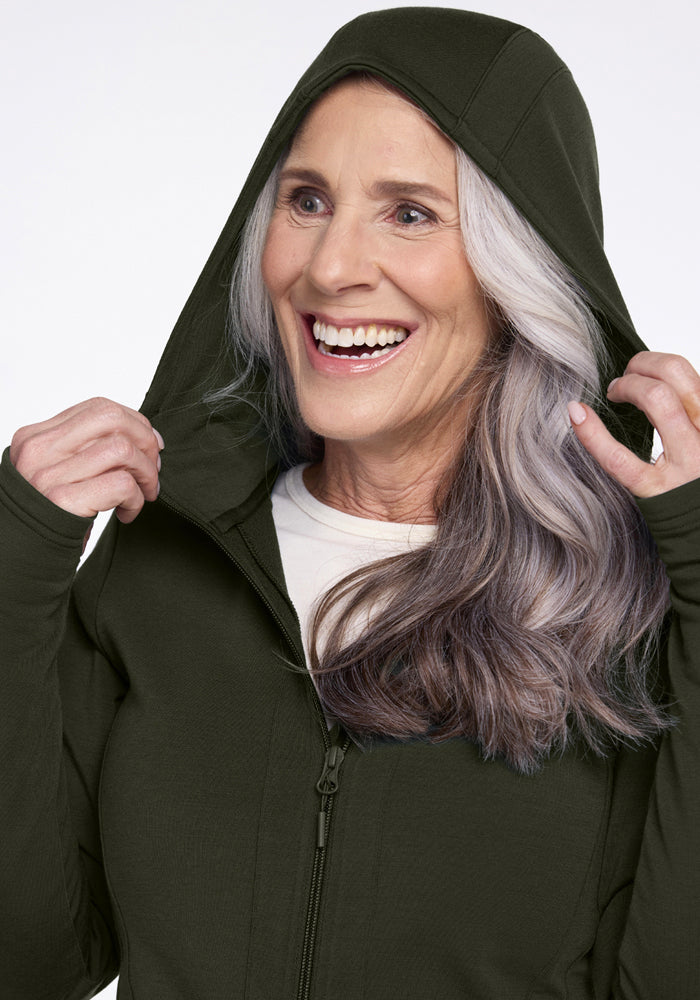 Smiling older woman in a Woolx Zoey Zip Up Hoodie - Duffel Bag, lifting the hood, ready for cold weather.