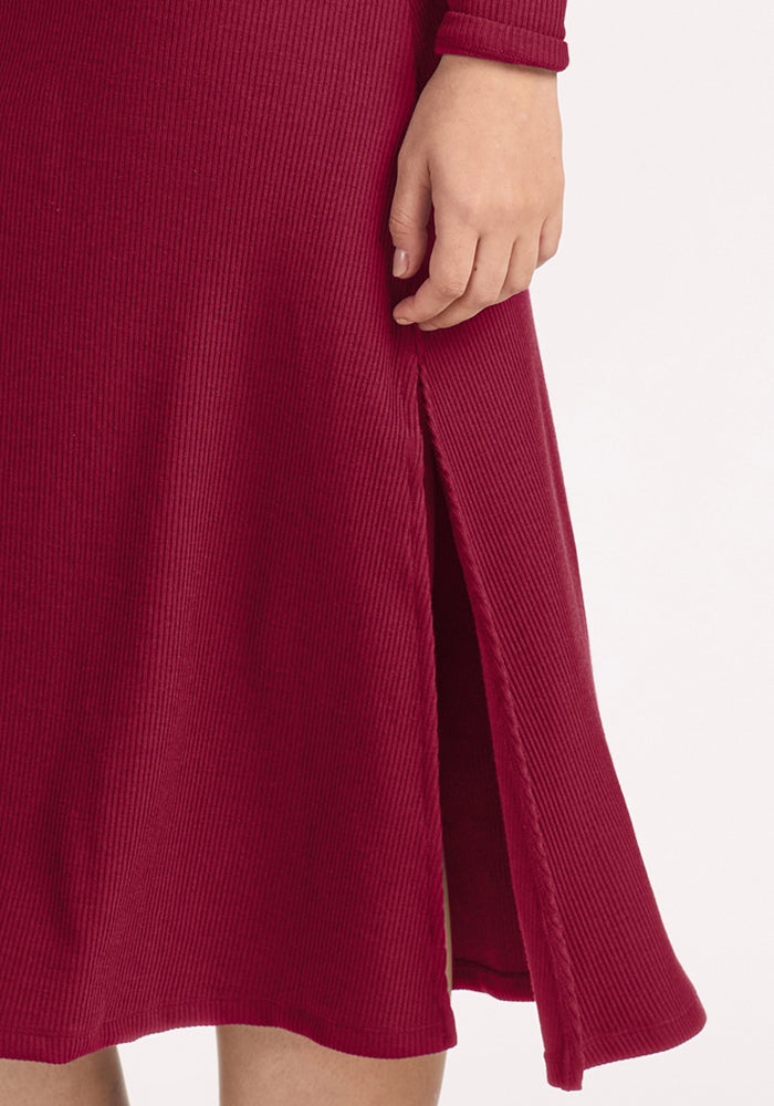 A person in the Woolx Caroline Ribbed Twirl Dress - Beet Red, long-sleeved with a side slit, shows their hand.