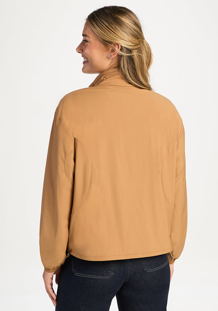 A woman wears a tan, high-collared, all-season Cooper Windbreaker - Saddleback, shown from the back.