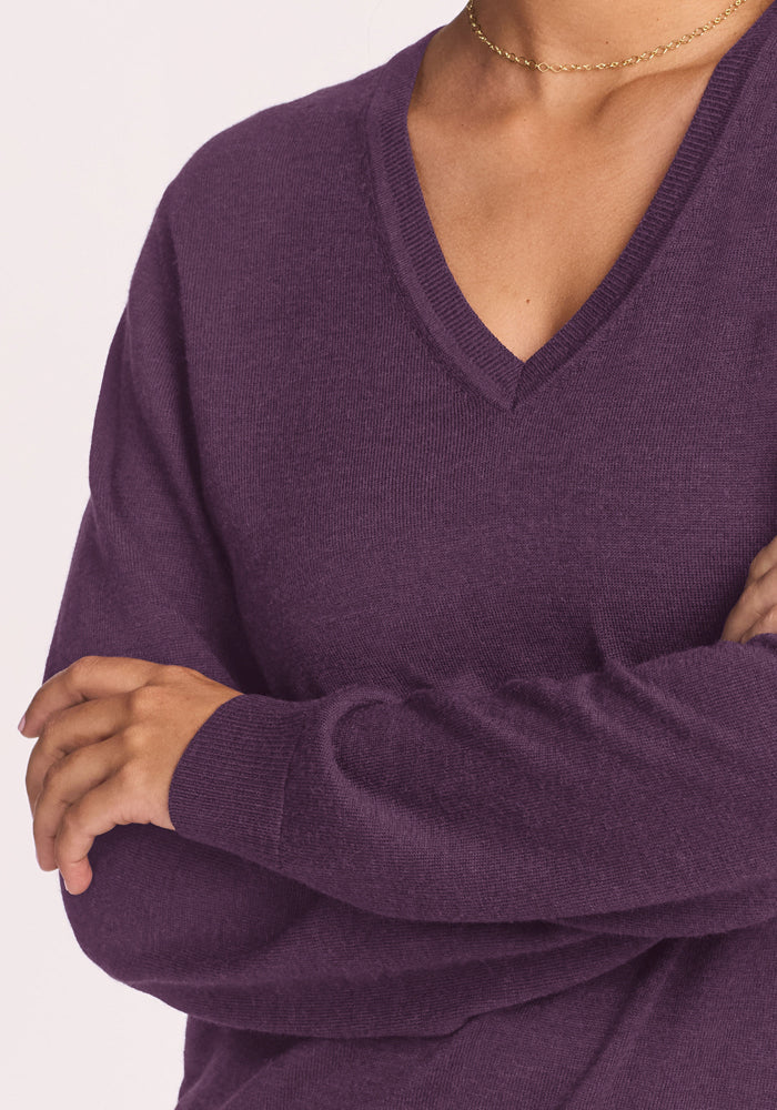 Model wears the Woolx Francesca Sweater in Purple Iris with a slim gold necklace, arms crossed, on a light background.