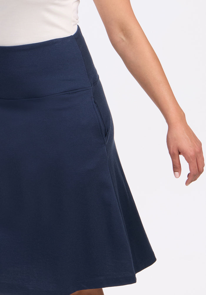 A person wearing the Woolx Marilyn Flowy Midi Skirt in Deep Navy with pockets and a white top, shown from the waist down with one arm relaxed at their side.