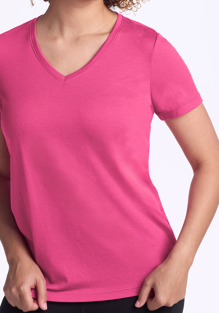 A person models the Woolx Junie V Neck in Raspberry Fizz, a short-sleeved relaxed fit t-shirt, standing with one hand on their hip against a plain light background. Their face is not visible.