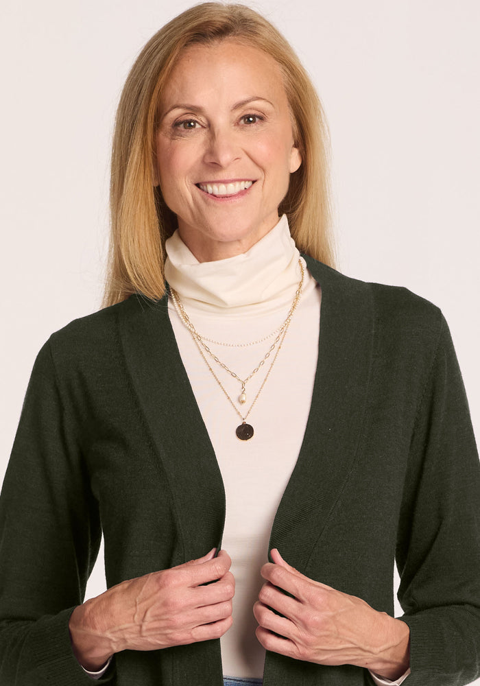 Smiling woman in Woolx Macie Sweater - Duffel Bag, cream turtleneck, and gold necklaces against a light background.