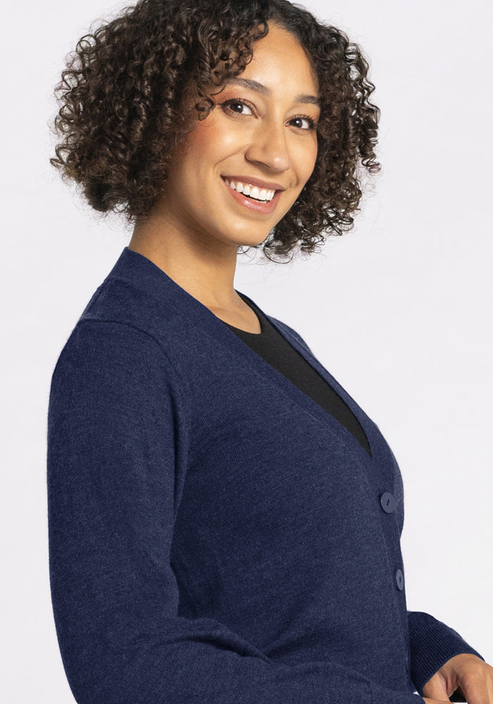 Smiling person with curly hair wears the Woolx Gia Sweater in Ocean Cavern over a black top, facing slightly sideways.