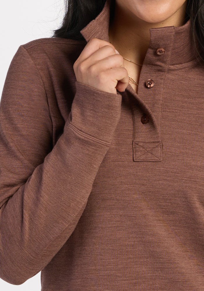 Woman in Woolx Annie 3 Button Pullover - Sable Heather, holding collar near face, shirt partially unbuttoned.