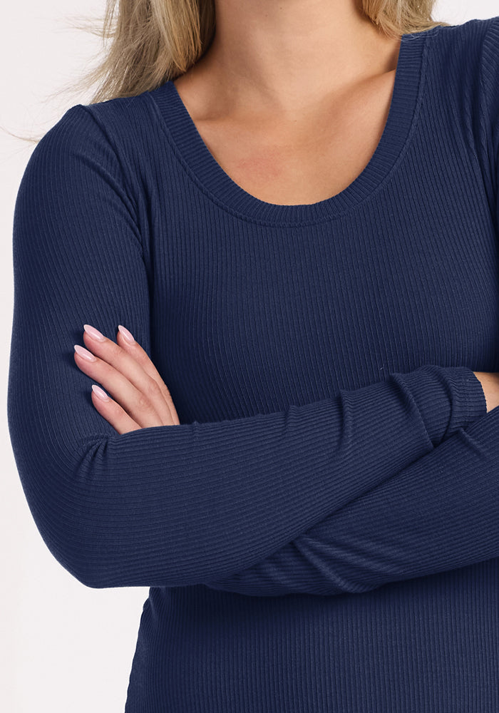 Individual with crossed arms in Woolx Caroline Ribbed Twirl Dress - Ocean Cavern, posing by a plain background.