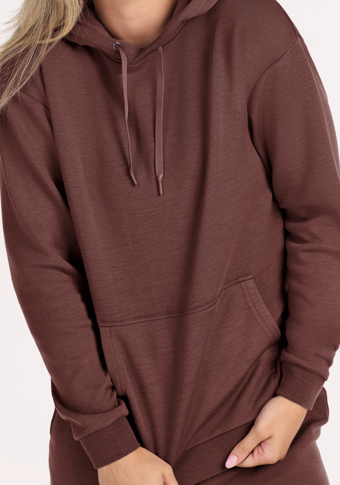 Person wears the Woolx Avery Hoodie in Canyon Clay, hands at waist, light pink nails, on a light background.