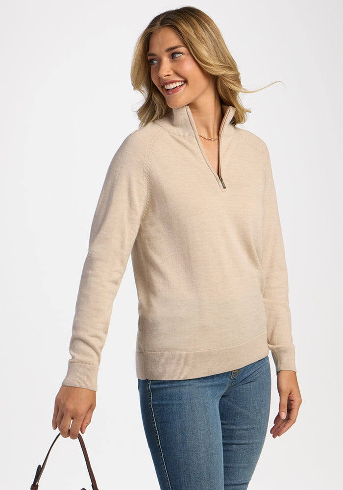 A woman smiles in a Woolx Collins Half Zip Sweater - French Oak, holding a bag against a white background.
