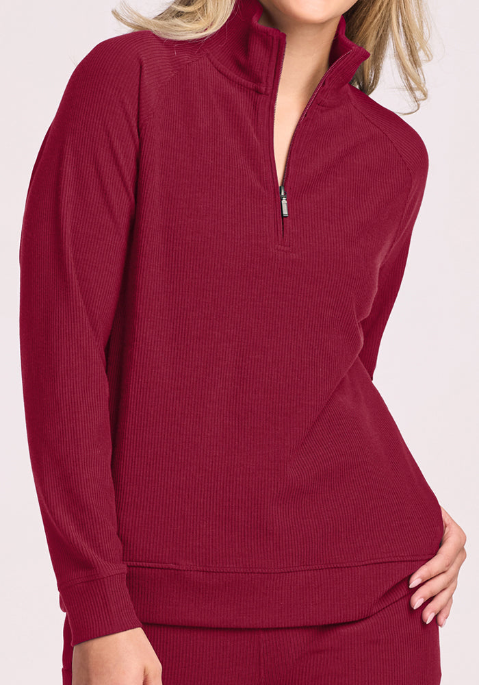 Woman wears the Woolx Quinn Ribbed 1/4 Zip in Beet Red with matching pants, hand on hip, radiating casual confidence.