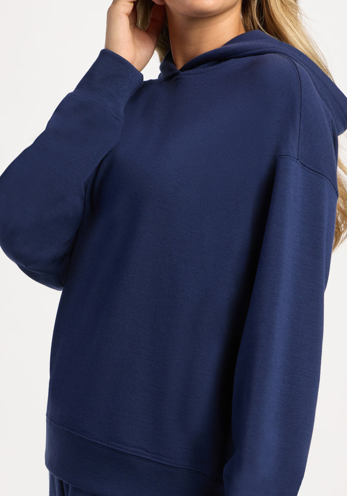 A person wearing a dark blue, long-sleeved, moisture-wicking Woolx Genevieve Hoodie - Ocean Cavern.