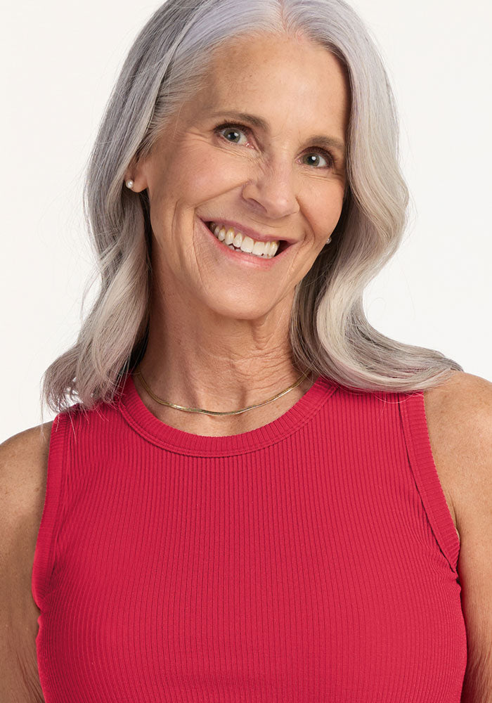 Smiling older woman in Woolx Raegan Ribbed Tank Top - Berry Ice Pop, gold necklace, long gray hair, white background.