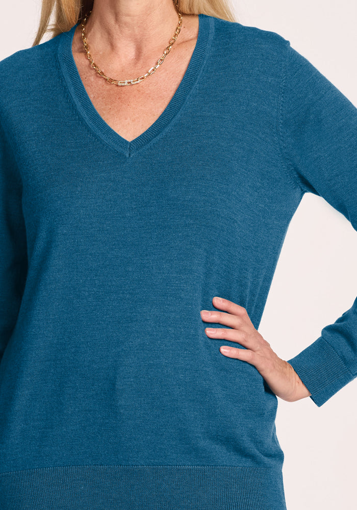 Woman in a Blue Pine Francesca Sweater by Woolx, gold chain necklace, hand on hip, set against a light background.
