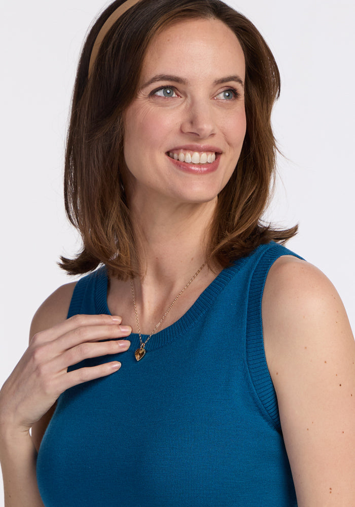 Woman with shoulder-length brown hair and a tan headband smiles while wearing the Woolx Chessy Tank Top in Moroccan Blue and a gold heart pendant, perfect as a stylish layering piece.