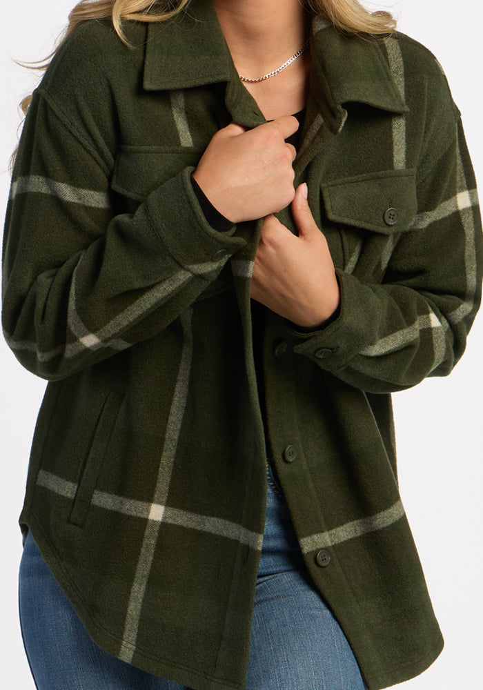 Person wears the Woolx Sawyer Shacket in Driftwood Fern Plaid with blue jeans, holding the cozy jacket closed with one hand.
