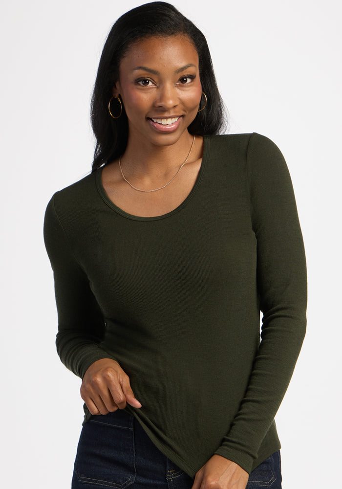 Woman in Woolx Katie Ribbed Long Sleeve - Duffel Bag and jeans, smiling with one hand at her waist on plain background.