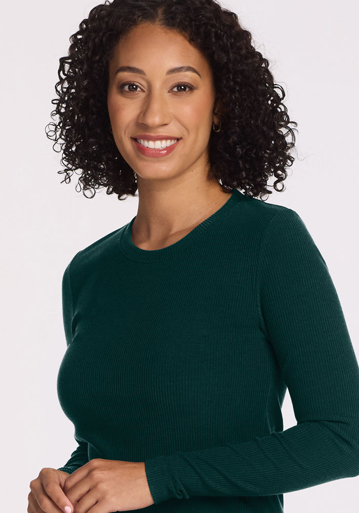 Smiling woman with curly hair wears the Woolx Hadley Ribbed Crew in Deep Pine, posing against a light background.