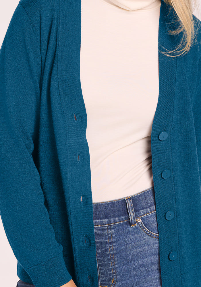 Person wearing Woolx Gia Sweater - Blue Pine over a white shirt and blue jeans, shown from neck to waist.