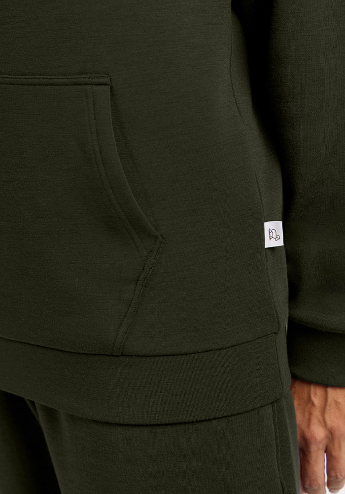 Close-up of a person wearing the Woolx Avery Hoodie - Duffel Bag with a kangaroo pocket and side tag.