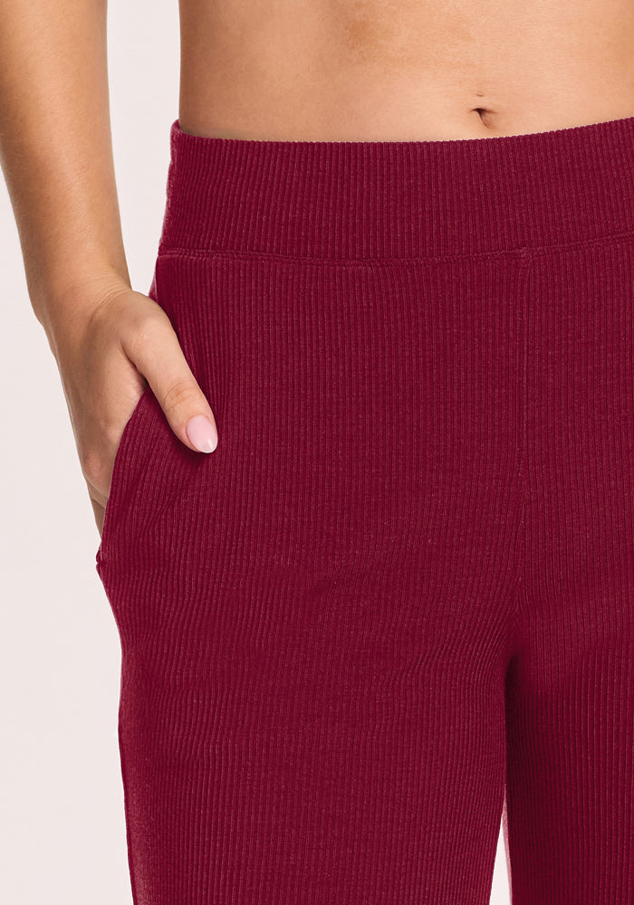 Model in Woolx Luca Ribbed Pants - Beet Red, high-waisted wide leg, hand in pocket, showcasing bare midriff.