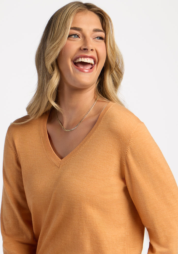 Smiling woman in the Woolx Francesca Sweater in Butterscotch and gold necklace, against a light background.