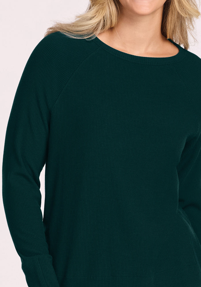 Woman in Woolx Ainsley Sweater - Deep Pine, shown shoulder to mid-torso, with wavy blonde hair.