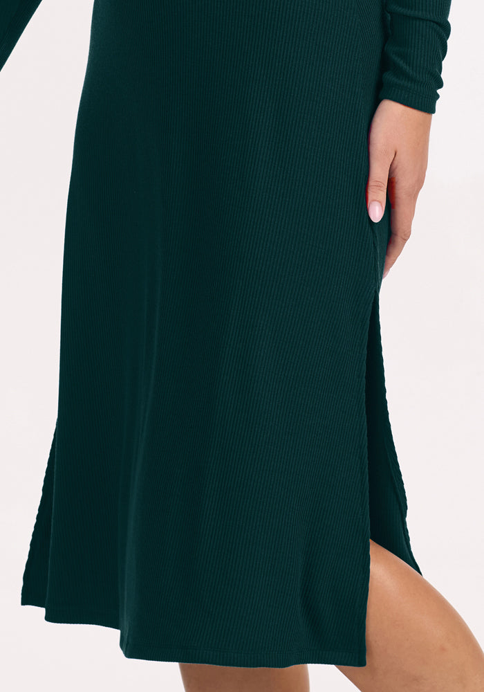 Person wearing Woolx Caroline Ribbed Twirl Dress in Deep Pine, showcasing its side slit, leg, and hand.