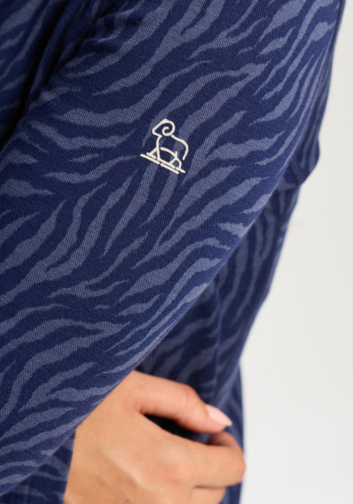 Close-up of Woolx Emi 1/4 Zip - Midnight Safari sleeve with zebra print and a white elephant logo.