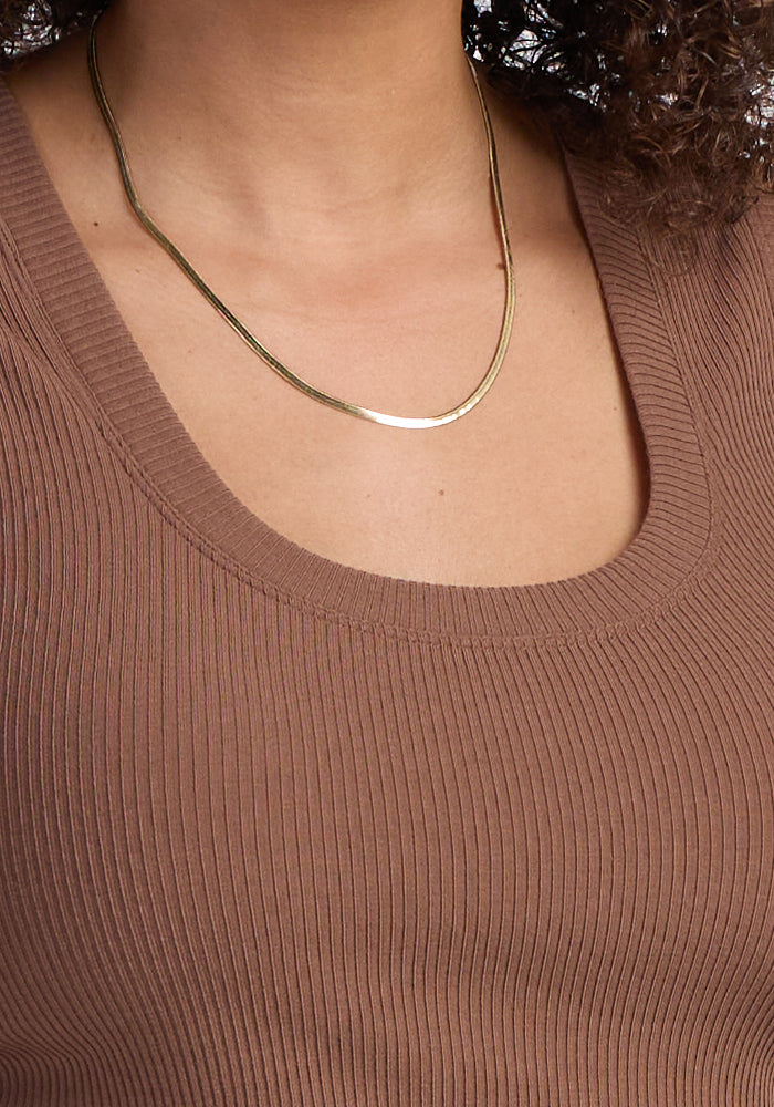A person wearing the Woolx Sloane Ribbed Tank in Sienna Kiss, featuring a scoop neck, paired with a simple gold chain necklace. Only the neck, collarbone, and upper chest are visible.