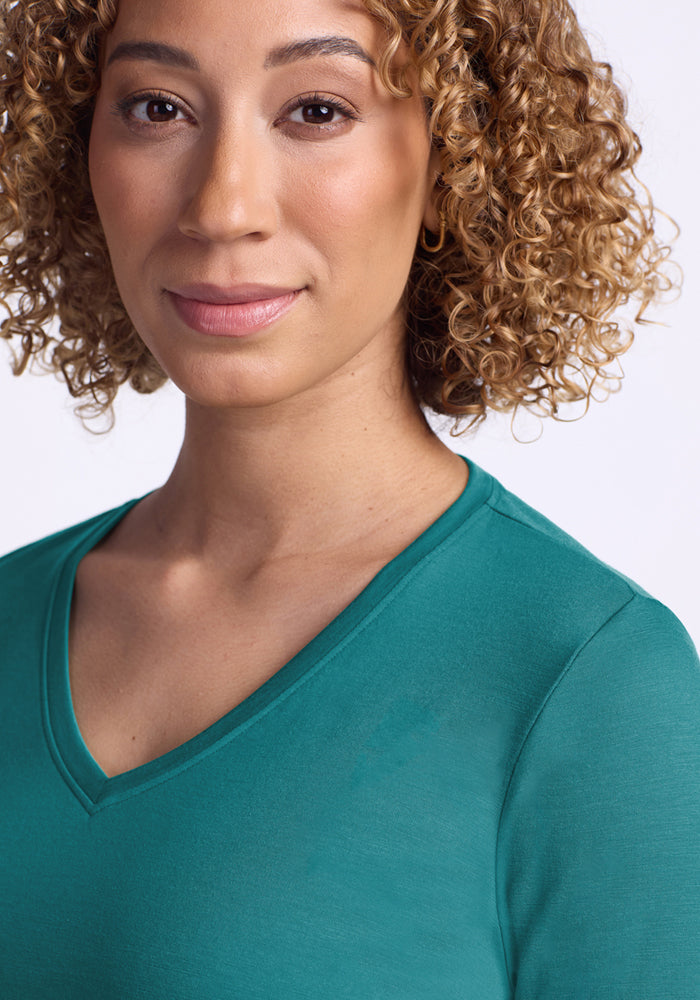 A woman with light brown curly hair, wearing the Woolx Millie Long Sleeve - Surfside top, smiles slightly at the camera against a plain white background.