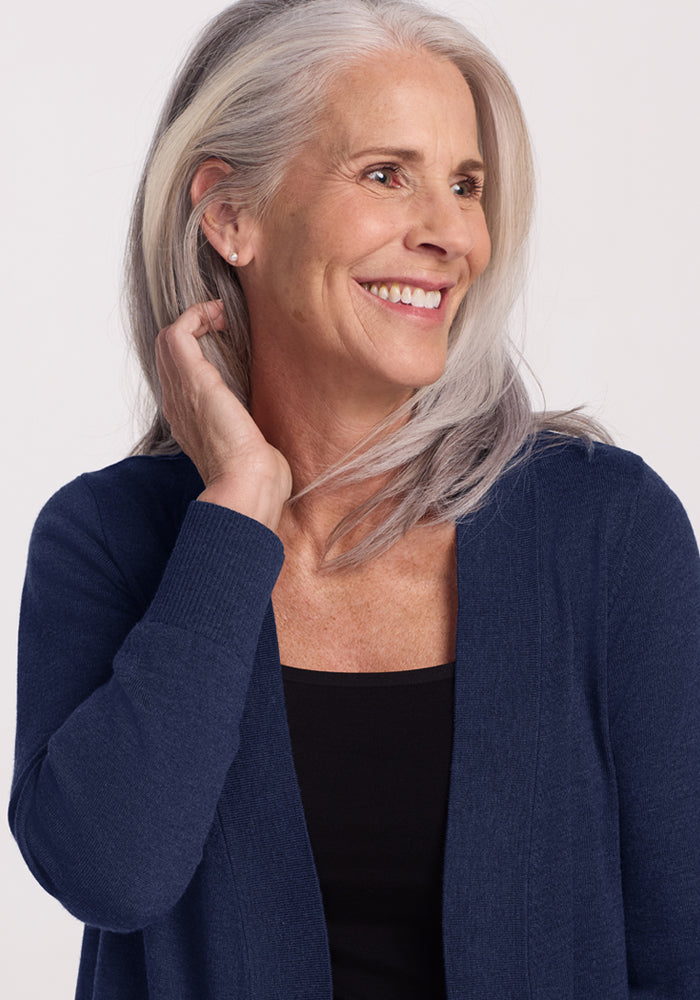 Smiling older woman in a Woolx Macie Sweater - Ocean Cavern touches her gray hair, wearing a black top.