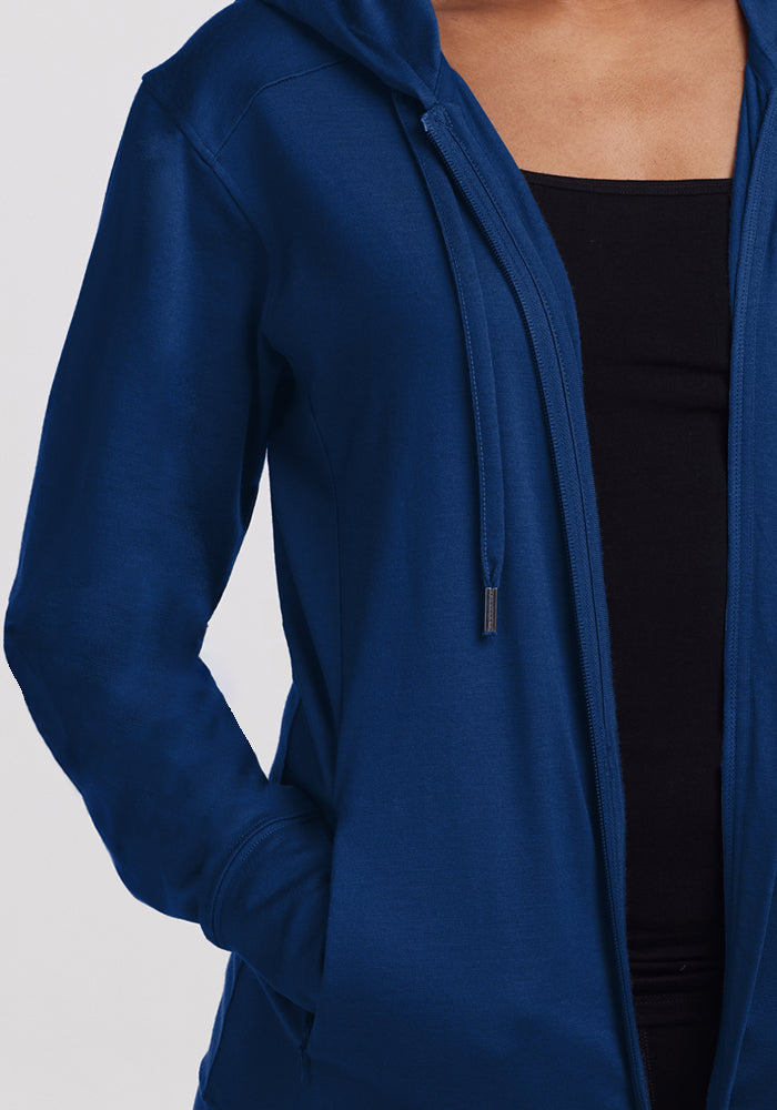 A person wears the Woolx Ryann Hoodie in Estate Blue over a black top, with one hand in the pocket. The image is cropped at the upper chest and does not show their face—making this hoodie a must-have travel essential.