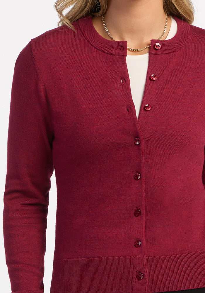 A woman wears the Woolx Caitlin Sweater in Beet Red, one button fastened over a white top, with a gold chain necklace.