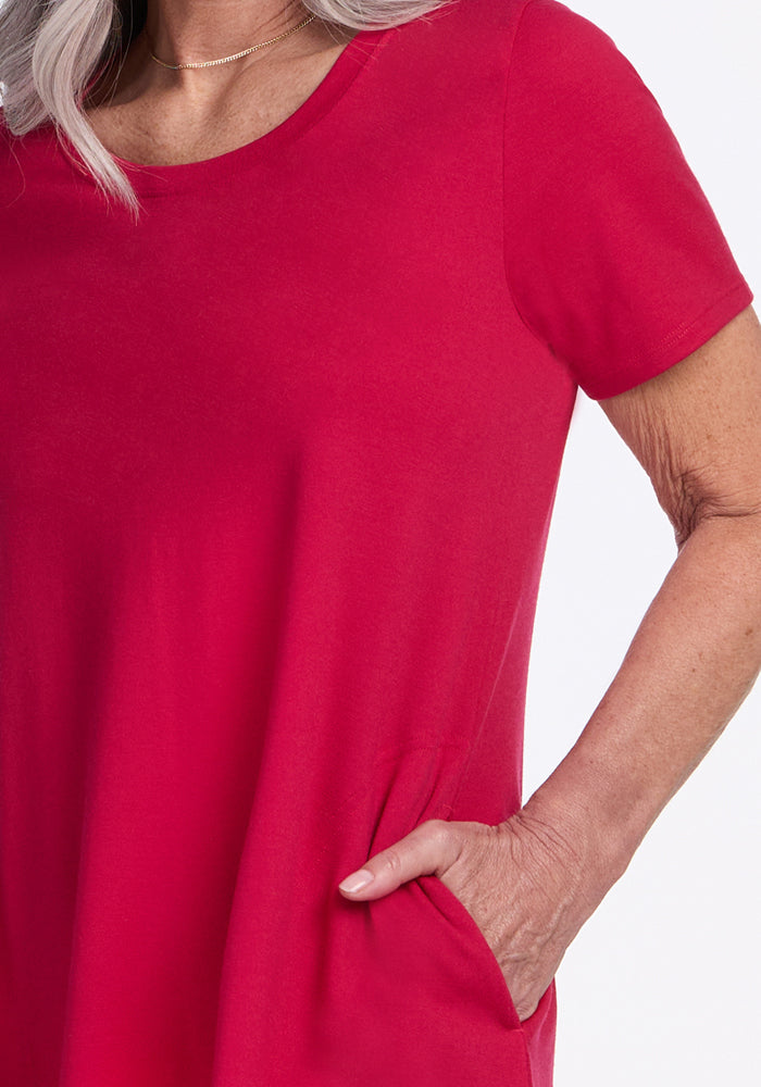 A woman wears the Woolx Georgie Dress in Poppy Spark, with her hand in the pocket. Only her upper torso and part of her arm are visible against a white background.