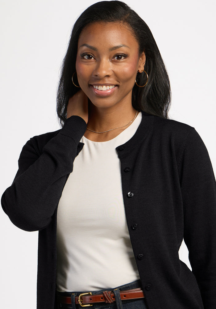 Smiling woman in a Woolx Caitlin Sweater - Black over a white shirt, hand on neck, with plain background.