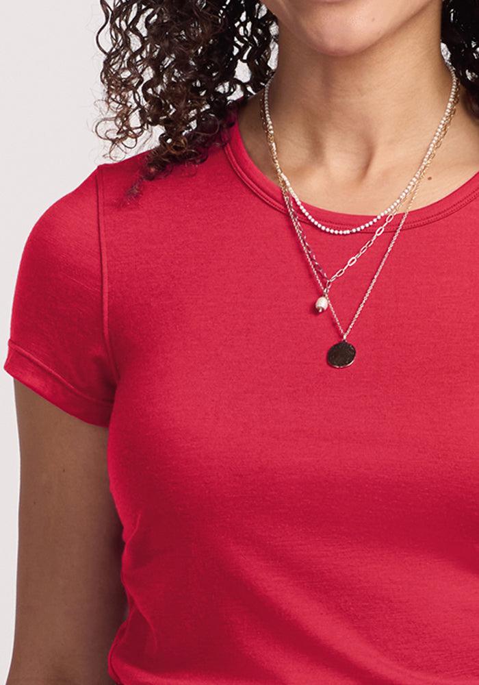 Woman wearing the Woolx Addie Crew Neck - Berry Ice Pop T-shirt and layered necklaces, with curly hair visible.
