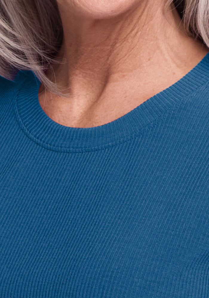 Close-up of a woman's lower face, neck, and shoulder wearing the Woolx Delia Ribbed Short Sleeve in Moroccan Blue. Her skin shows light wrinkles and a few gray hairs are visible near her neck.