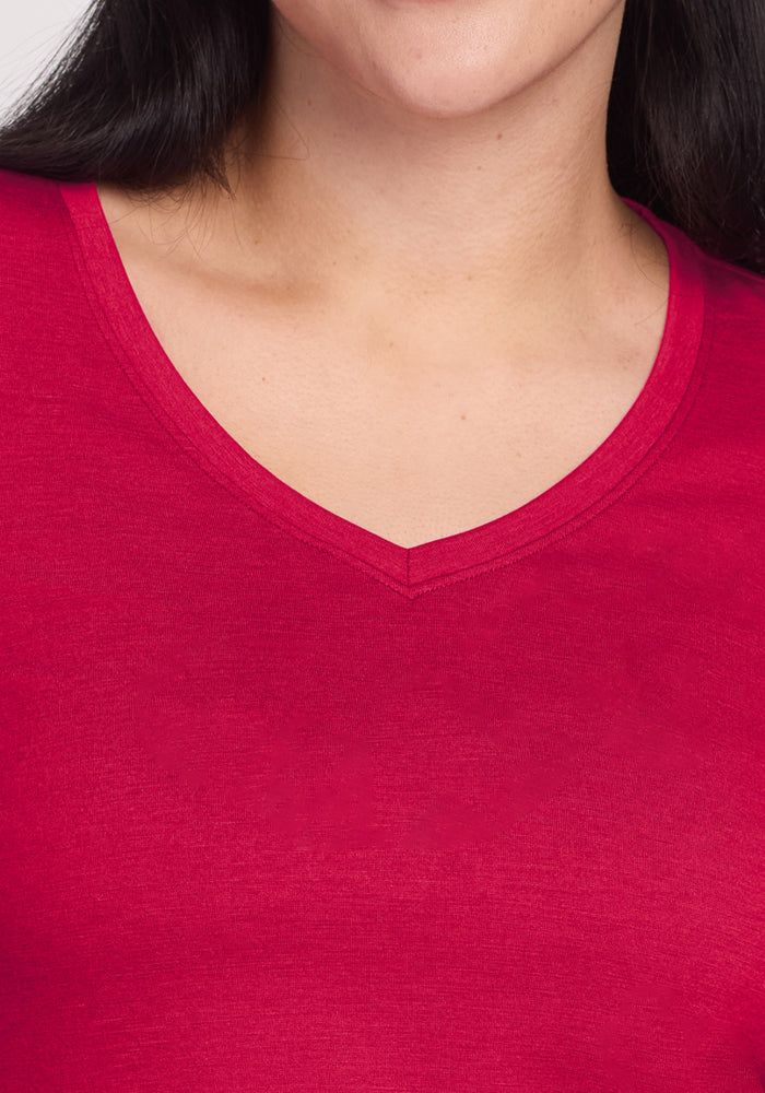 Close-up of a person wearing the Woolx Millie Long Sleeve in Poppy Spark, a bright red moisture-wicking Merino wool top with a V-neck. Part of the face and long dark hair are visible, focusing on the neckline and upper chest.