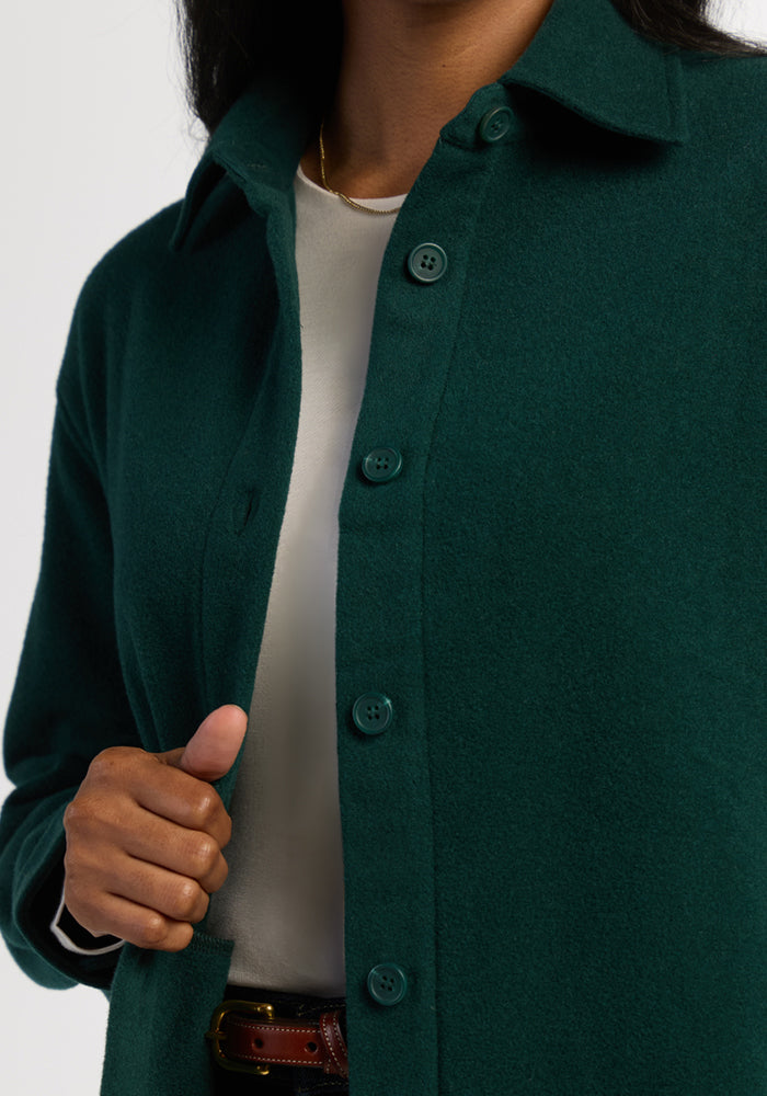 Close-up of a person in the Woolx Jovie Shacket - Deep Pine, layered over white and holding the edge of the cozy jacket.