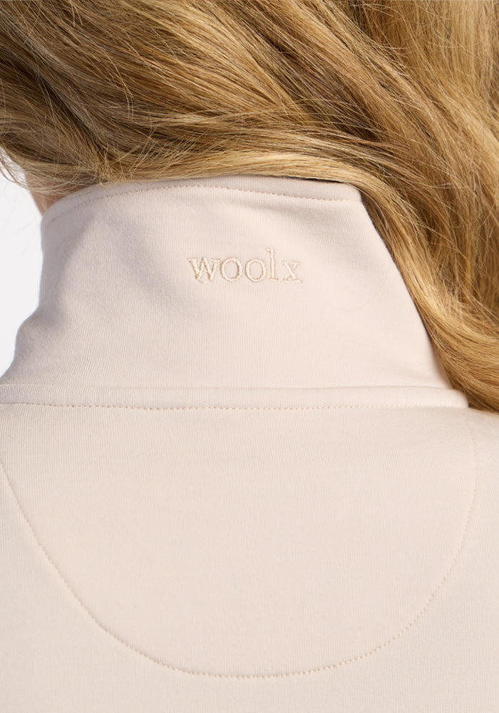 Back view of blonde hair, wearing Woolx Finley Zip Up Sweatshirt in ecru, “woolx” logo on the collar.