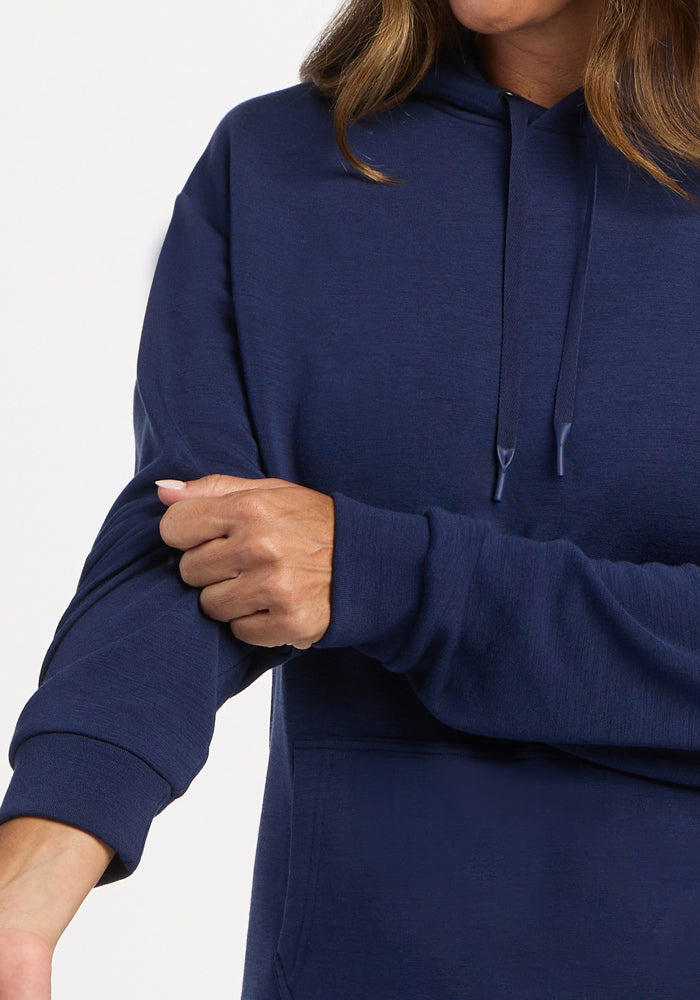 Woman in a Woolx Avery Hoodie - Ocean Cavern scrunches her left sleeve, with only her mouth partially visible.