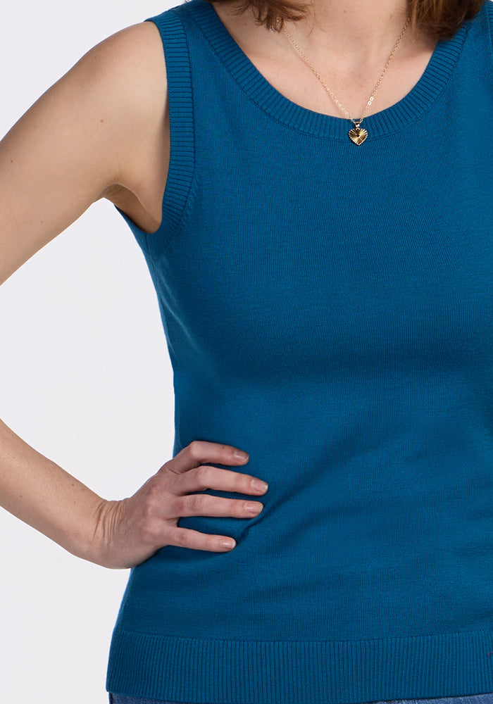 A woman wears the Woolx Chessy Tank Top in Moroccan Blue and a gold heart-shaped necklace, standing with one hand on her hip against a plain white background.