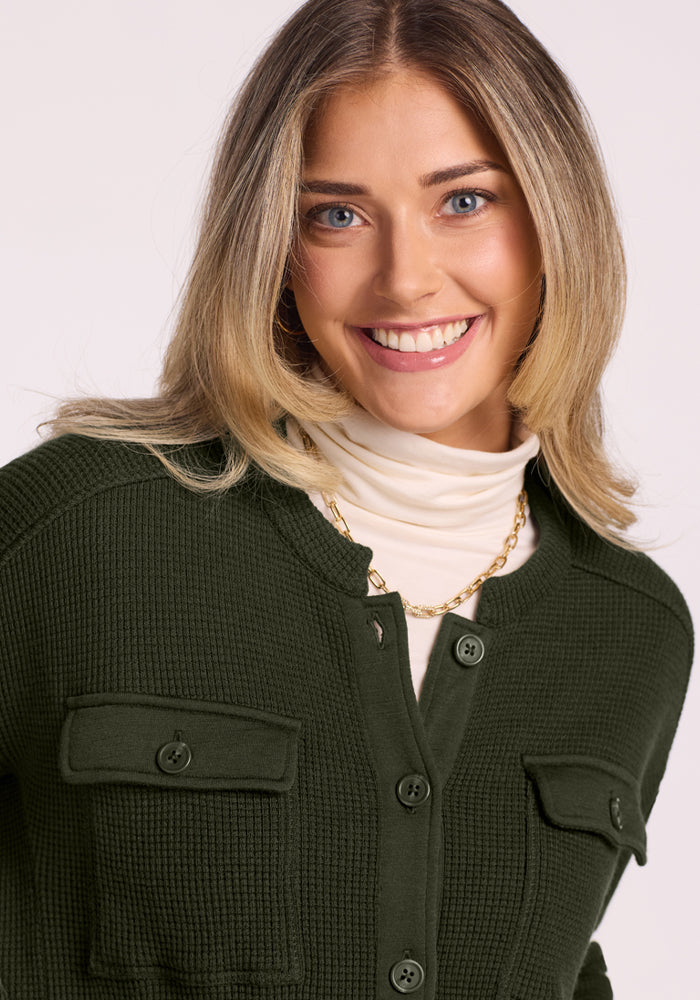 Smiling woman in the Woolx Oaklynn Waffle Shacket - Duffel Bag over a cream turtleneck, gold chain, light background.