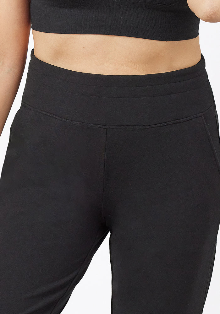A person is shown from mid-torso to mid-thigh wearing Woolx Madden Joggers - Black and a black crop top, set against a plain white background.